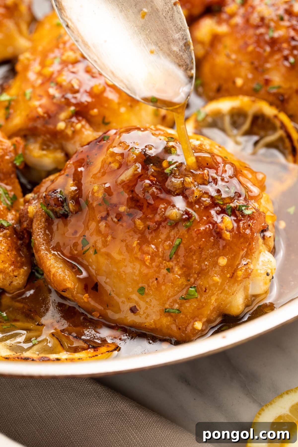A spoonful of sauce being drizzled over a honey garlic lemon pepper chicken thigh on a plate.