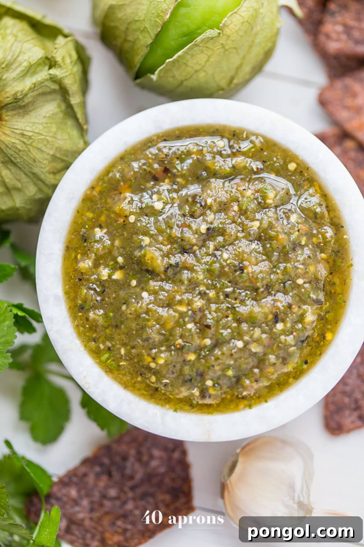 Top-down, overhead view of a small bowl of green roasted salsa verde surrounded by blue corn chips.