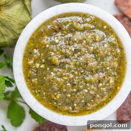 Top-down, overhead view of a small bowl of green roasted salsa verde surrounded by blue corn chips.