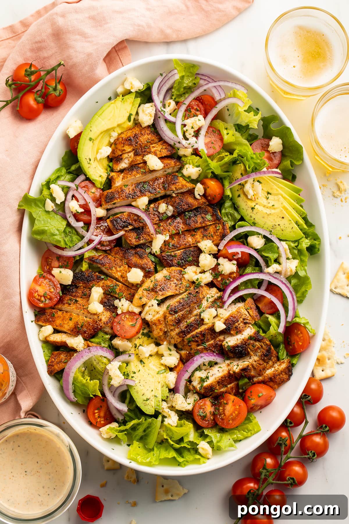 Top down view of an oval platter filled with cajun chicken salad - lettuce, cherry tomatoes, red onion, and ranch.
